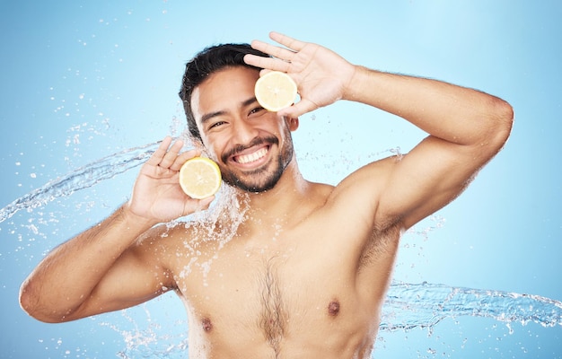 Acqua ritratto e limone con un modello di uomo in studio su uno sfondo blu per l'idratazione o l'igiene naturale Affronta la frutta e la bellezza con un bel giovane maschio bagnato da una spruzzata d'acqua nel bagno