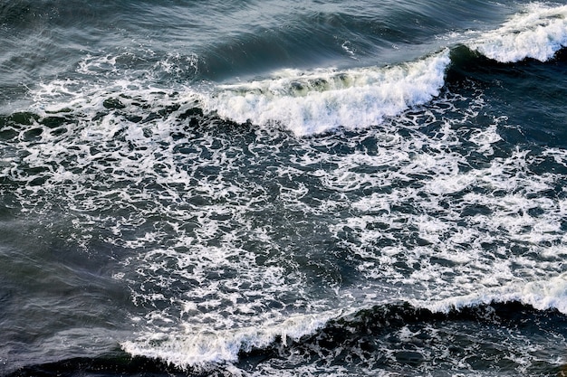 Acque di mare blu profondo che spruzzano con onde spumose. Vista aerea delle onde di spruzzi dell'oceano, acque di mare ondulate blu scuro con schiuma bianca. Superficie dell'acqua, mare in tempesta. Sfondo naturale, copia spazio