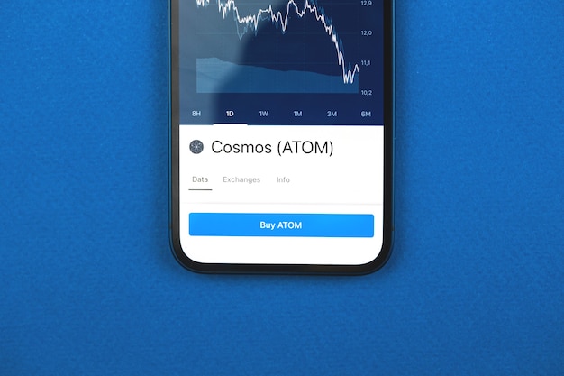 Acquista la criptovaluta Cosmos ATOM tramite l'app per telefono cellulare, il concetto di commercio online, gli investimenti e lo scambio di monete con smartphone, foto aziendali e finanziarie