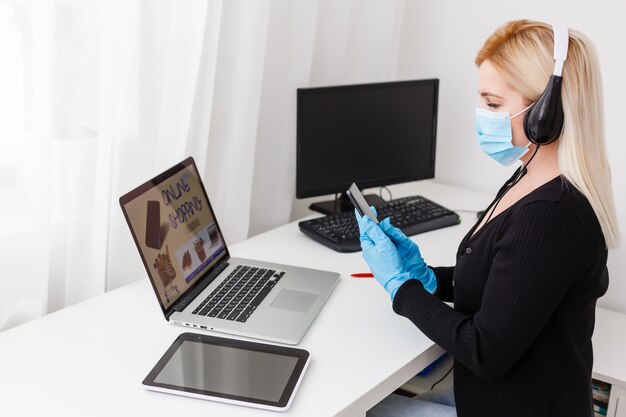 Acquisti online durante la quarantena del coronavirus. Donna in maschera protettiva a casa, spazio libero