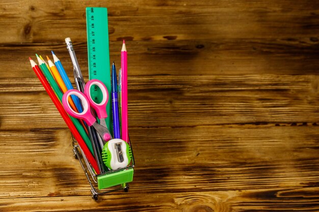 Acquisto di materiale scolastico Carrello con materiale scolastico su sfondo di legno Torna al concetto di scuola