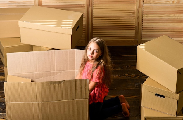 Acquisto di una nuova abitazione bambina felice seduta nella stanza sulle scatole riparazione della stanza nuovo appartamento disimballaggio delle scatole per il trasloco bambino felice scatola di cartone Scatole di cartone La casa è dove si trova il cuore