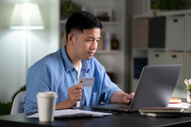Acquisto online dell'uomo asiatico utilizzando il computer portatile e tenendo la carta di credito