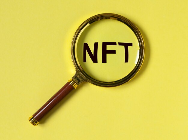 Acronimo Nft tramite lente di ingrandimento su sfondo giallo