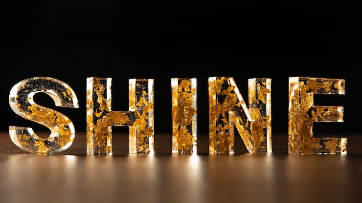 Photo acrylic letters with gold leaves forming the word shine on wooden surface, black background, selective focus.