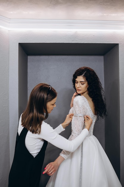 Adattamento femminile all'abito da sposa in studio di stilista Sposa che indossa il suo abito da sposa con designer di abiti femminili che effettua le regolazioni finali sul vestito