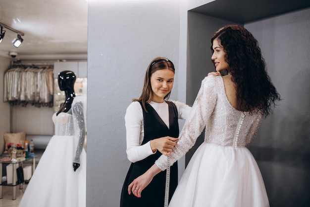 Adattamento femminile all'abito da sposa in studio di stilista Sposa che indossa il suo abito da sposa con designer di abiti femminili che effettua le regolazioni finali sul vestito