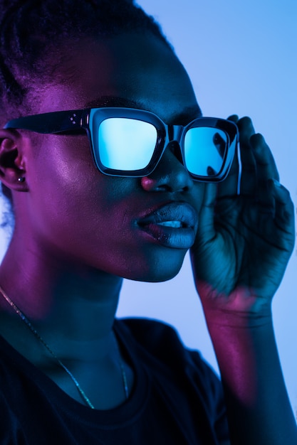 Adatti i giovani vetri africani di usura della donna della ragazza che esaminano la macchina fotografica isolata sullo spazio al neon