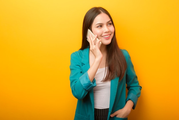 Adatti il ritratto di bella donna in vestito verde facendo uso del cellulare su giallo