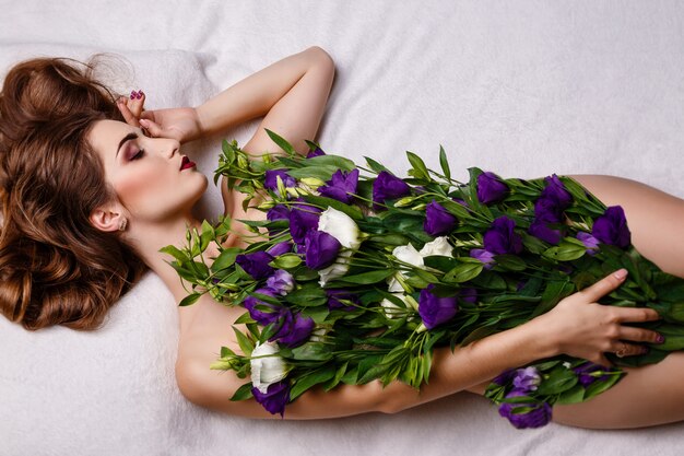 Adatti la foto dello studio di bella donna castana con trucco luminoso con un mazzo dell'eustoma porpora e bianco