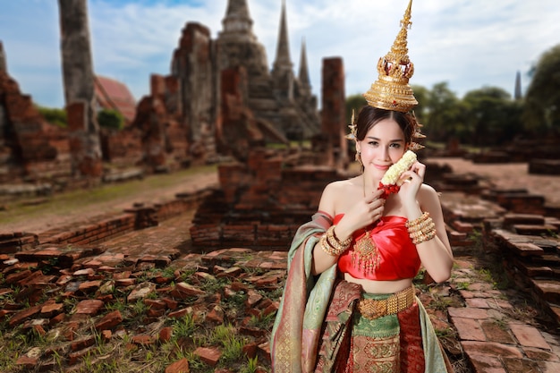 Adatti la ragazza asiatica in costume tradizionale tailandese in tempio antico con il fiore del volante a disposizione