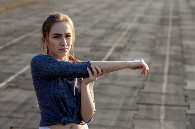 Addestramento della giovane donna sullo stadio di estate. Sportiva, stretching, riscaldamento prima dell'allenamento all'aperto. Uno stile di vita sano