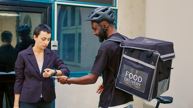 Addetto al servizio di consegna che dà fastfood in un sacchetto di carta a una donna, cliente che paga l'ordine utilizzando smartwach con nfc. Corriere maschio che consegna il pranzo, pagamento senza contatto pos. Tiro a mano libera.