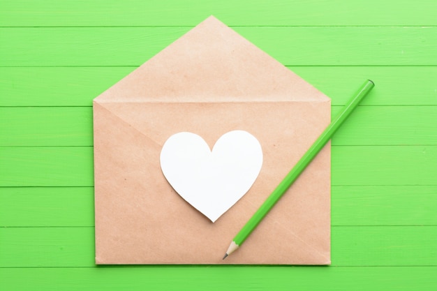 Adesivo bianco a forma di cuore in una busta su fondo di legno verde