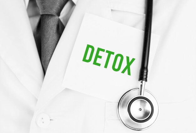 Adesivo bianco con testo DETOX sdraiato sulla veste medica con uno stetoscopio