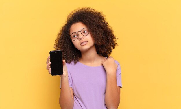 Adolescente abbastanza afro che si sente stressato, ansioso, stanco e frustrato, tira il collo della camicia, sembra frustrato dal problema e tiene in mano una cella