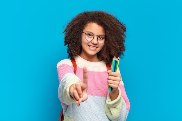 Adolescente abbastanza afro che sorride con orgoglio e sicurezza facendo posare trionfante il numero uno