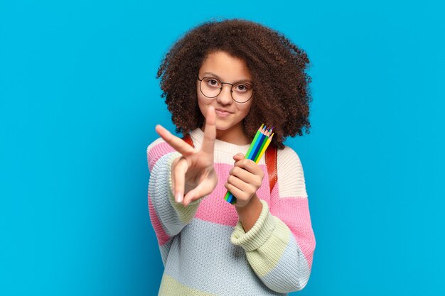 Adolescente abbastanza afro che sorride e sembra felice, spensierato e positivo, gesticolando vittoria o pace con una mano. concetto di studente