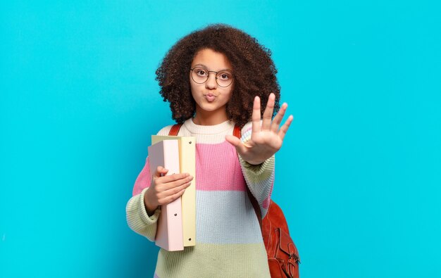 Adolescente abbastanza afro sorridente e dall'aspetto amichevole, mostrando il numero cinque o il quinto con la mano in avanti, conto alla rovescia. concetto di studente