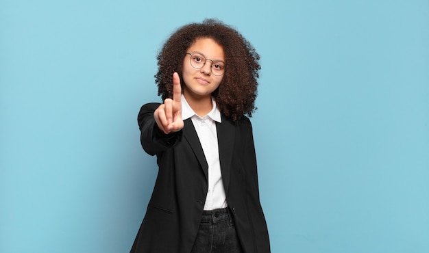 Adolescente abbastanza afro sorridente e dall'aspetto amichevole, mostrando il numero uno o il primo con la mano in avanti, conto alla rovescia