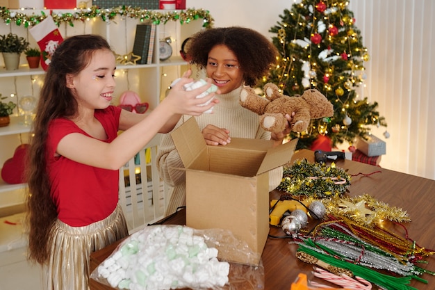 Adolescente allegra che prende la neve finta fuori dalla scatola con le decorazioni di Natale