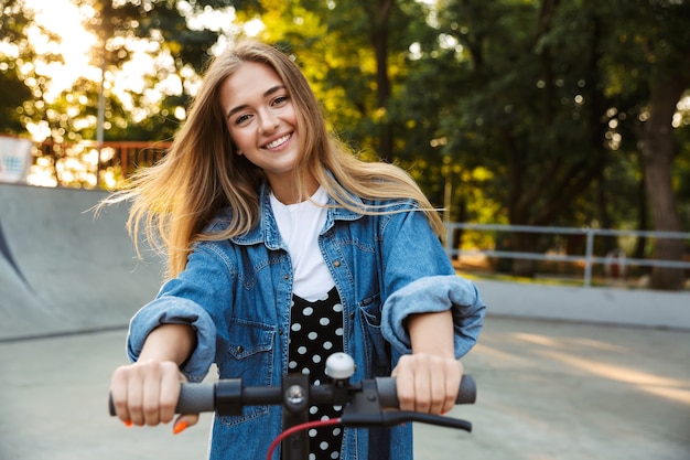 adolescente allegro sorridente felice in parco che cammina sul motorino.