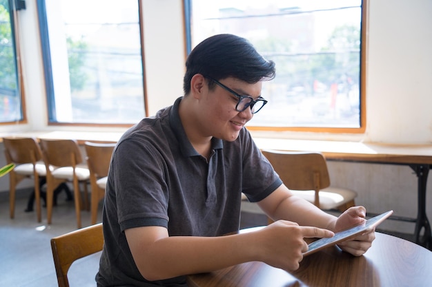 Adolescente asiatico felice che utilizza smartphone e tablet presso la caffetteria Uomo asiatico che tiene tablet chiama mamma