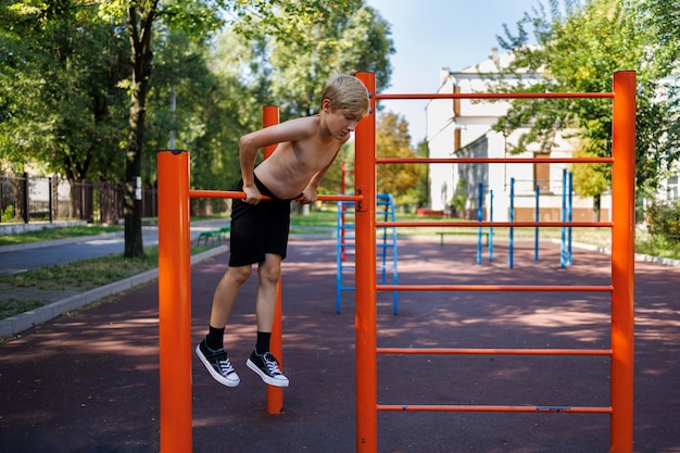 Adolescente atleta tiene le mani sul traverso appeso su di esso allenamento di strada su una barra orizzontale nel parco della scuola