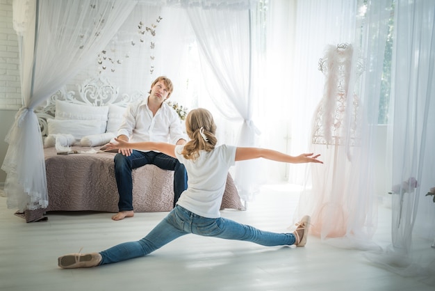 adolescente ballerina si attorciglia sul pavimento di fronte a un padre stanco seduto sul letto