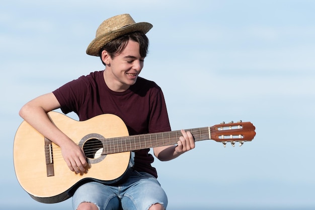 Adolescente bello che indossa un cappello di paglia che suona la chitarra all'aperto