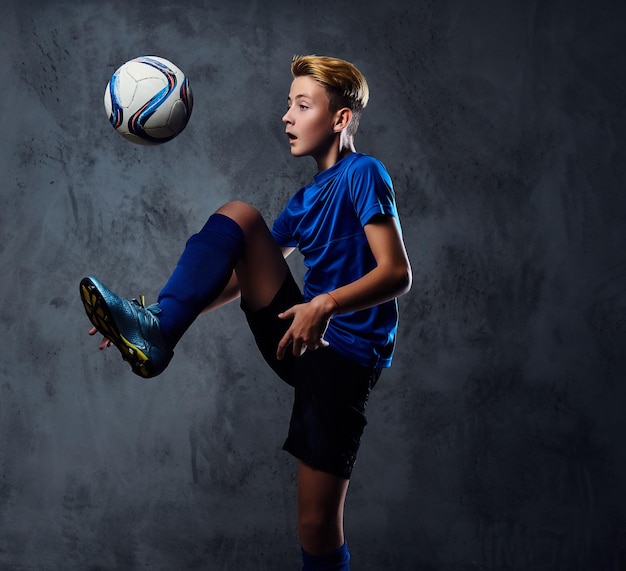 Adolescente bionda, giocatore di calcio vestito con un'uniforme blu gioca con una palla.