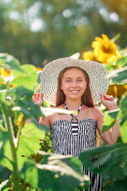 Adolescente carina con un cappello a tesa larga in un campo di girasoli. Concetto di ora legale.