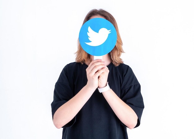 Adolescente caucasico che tiene in mano un'immagine del logo di Twitter su uno sfondo bianco
