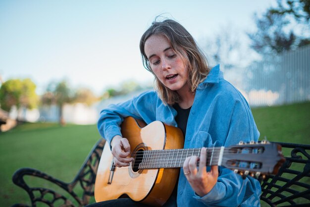 Adolescente che canta e suona la chitarra su una panchina