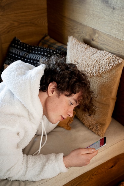 Adolescente che cerca qualcosa su Internet usando il suo smartphone mentre è seduto sul suo letto