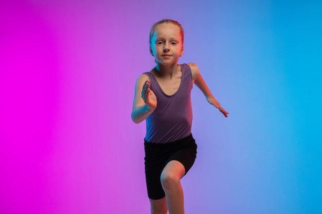 Adolescente che corre, fa jogging sullo sfondo dello studio al neon rosa-blu sfumato in movimento
