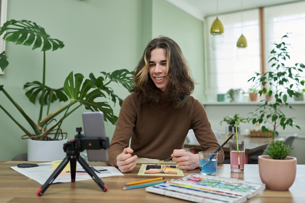 Adolescente che disegna con acquerelli guardando la lezione di video sullo smartphone