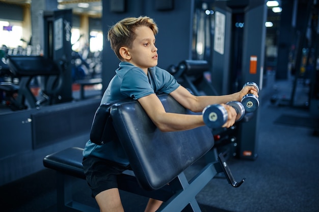 Adolescente che fa esercizio con manubri in palestra, vista laterale. Giovane in formazione in club sportivo, assistenza sanitaria e stile di vita sano, scolaro in allenamento, gioventù sportiva