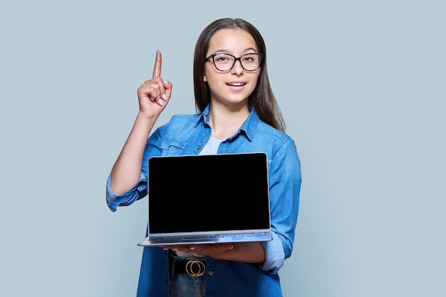 Adolescente che mostra lo schermo del laptop vuoto in posa su sfondo grigio