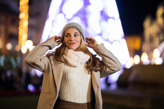 Adolescente che regola il suo cappello di notte con sciarpa in inverno. Sullo sfondo l'albero di Natale.