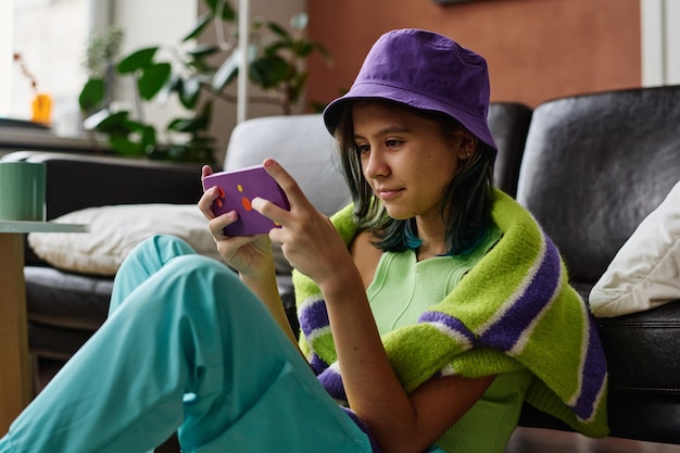 Adolescente che utilizza il suo smartphone per giocare online nel soggiorno di casa