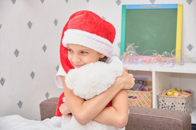 Adolescente cita ragazza abbraccia orsacchiotto bianco in maglione rosso, ragazza nella stanza decorata di natale