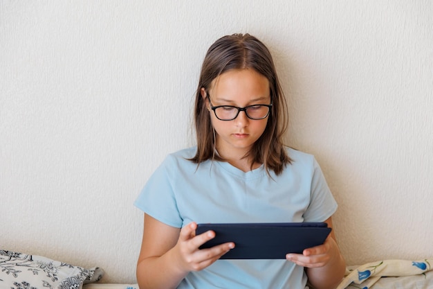 Adolescente con gli occhiali che gioca un tablet su un letto in camera da letto