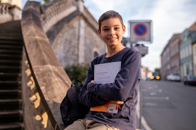 Adolescente dai capelli scuri carino felice sorridente con un libro che si siede sulla balaustra delle scale di cemento