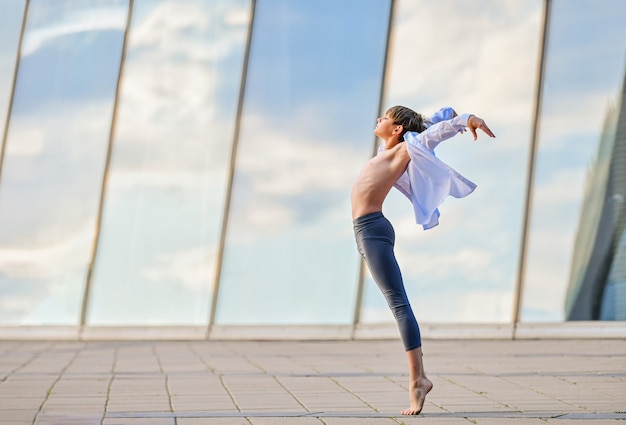 Adolescente del ragazzo di balletto che balla in modo espressivo sullo sfondo del riflesso del cielo nella parete di vetro