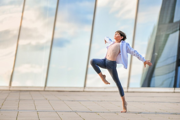 Adolescente del ragazzo di balletto che balla in modo espressivo sullo sfondo del riflesso del cielo nella parete di vetro