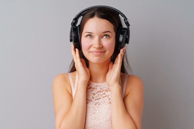 Adolescente della giovane donna che ascolta la musica con le sue cuffie sopra un fondo grigio