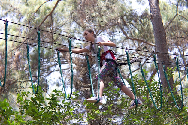 Adolescente della ragazza con attrezzatura rampicante in un parco di divertimenti della corda