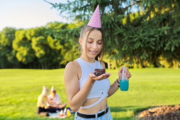 Adolescente di compleanno in cappello festivo con torta e candela alla festa all'aperto