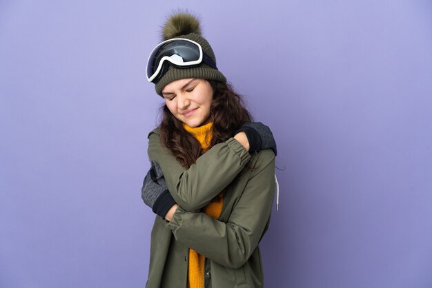 Adolescente donna russa con occhiali da snowboard isolato sulla parete viola soffre di dolore alla spalla per aver fatto uno sforzo